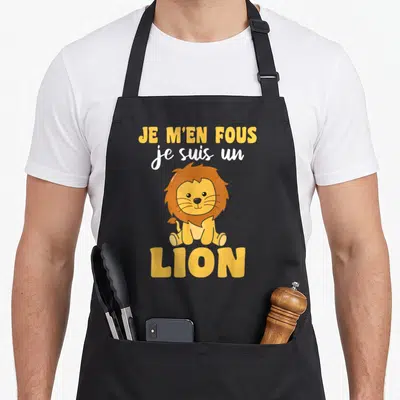 Tablier de cuisine noir avec un lion cartoon jaune et orange et le texte Je m'en fous je suis un lion