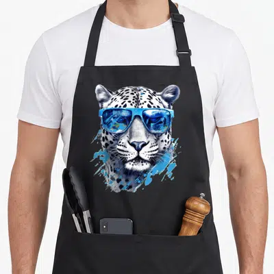 Tablier de cuisine noir avec tête de léopard blanc portant des lunettes de soleil bleues reflétant un paysage.