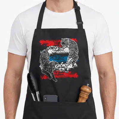 Tablier de cuisine noir avec illustration de deux tigres s'affrontant en Muay Thai sur un fond texturé rouge et bleu.