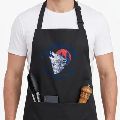 Tablier de cuisine noir avec illustration vintage d'un loup hurlant devant un soleil rouge et des arbres bleus.