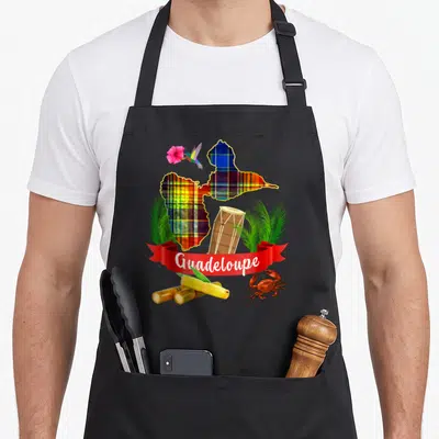 Tablier de cuisine noir avec une carte de Guadeloupe en madras, un tambour, un colibri, une fleur d'hibiscus, des tiges de canne à sucre et un crabe rouge.