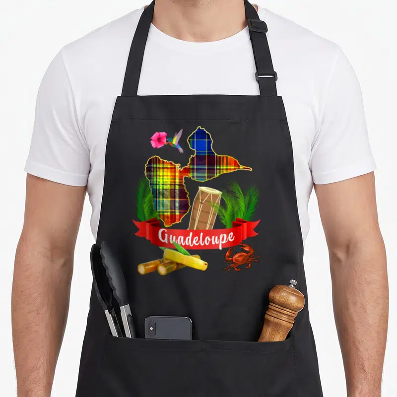 Tablier de cuisine noir avec une carte de Guadeloupe en madras, un tambour, un colibri, une fleur d'hibiscus, des tiges de canne à sucre et un crabe rouge.