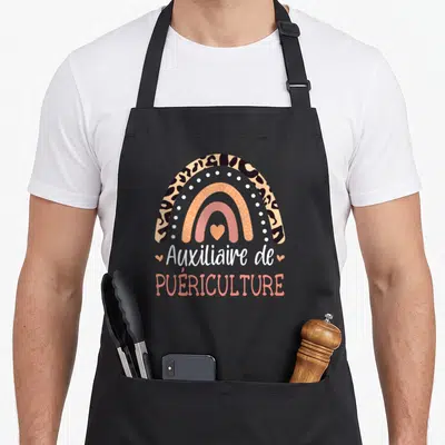Tablier de cuisine noir avec arc-en-ciel à motif léopard et texte Auxiliaire de Puériculture en typographie manuscrite et capitale.
