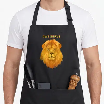 Tablier de cuisine noir avec tête de lion orange et texte #WE SERVE en haut.