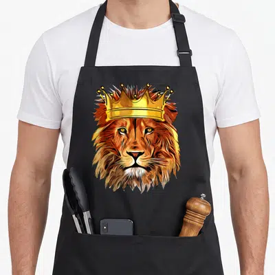 Tablier de cuisine noir avec une grande tête de lion couronnée aux tons dorés et orange vifs.