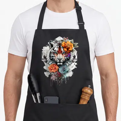 Tablier de cuisine noir avec tête de tigre aux yeux bleus, fleurs orange et bleues, motifs géométriques noirs et éclaboussures artistiques.