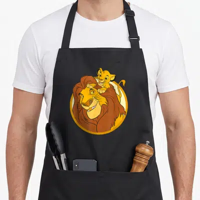 Tablier de cuisine noir avec illustration d'un grand lion portant un jeune lion sur sa tête dans un cadre circulaire.