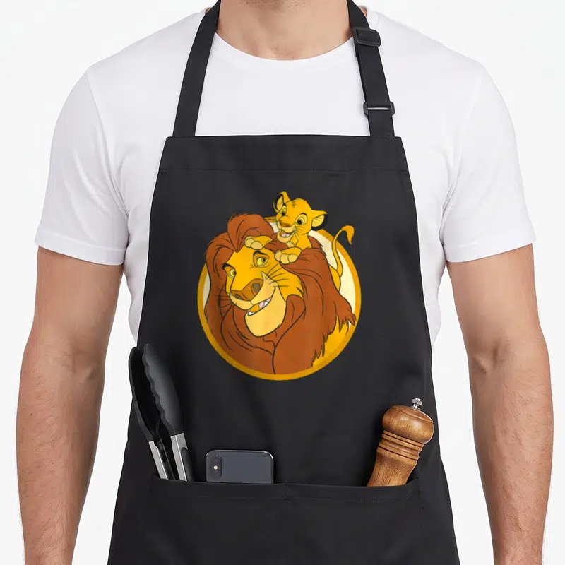 Tablier de cuisine noir avec illustration d'un grand lion portant un jeune lion sur sa tête dans un cadre circulaire.