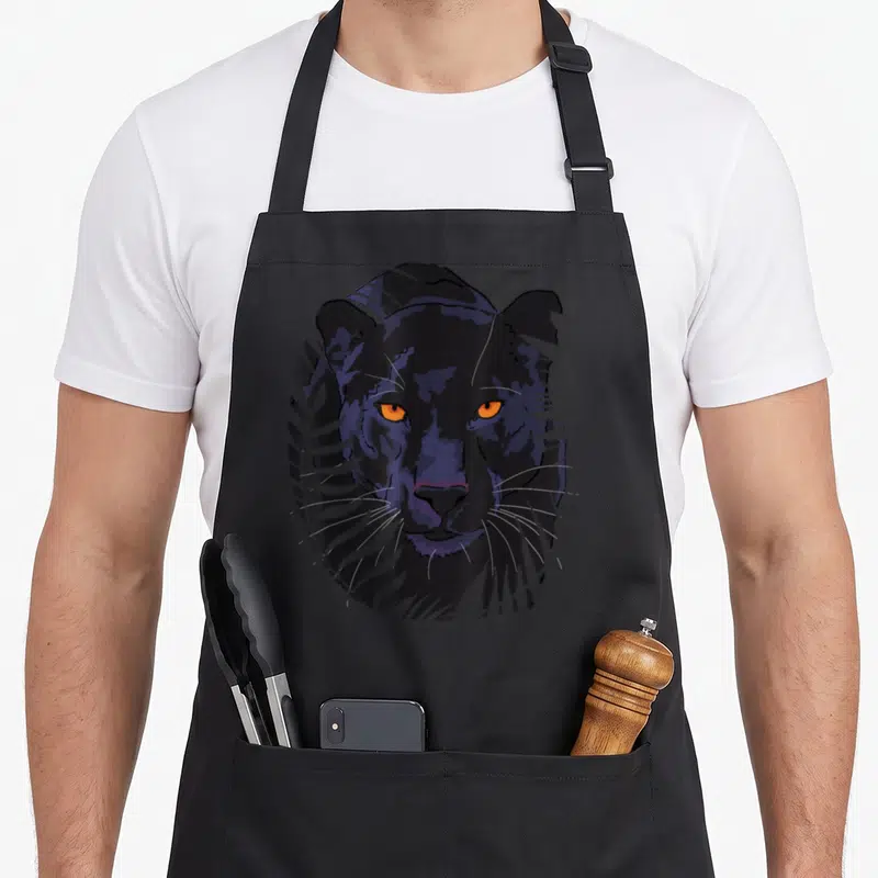 Tablier de cuisine noir avec une illustration de tête de panthère noire aux yeux orange et feuilles grises.