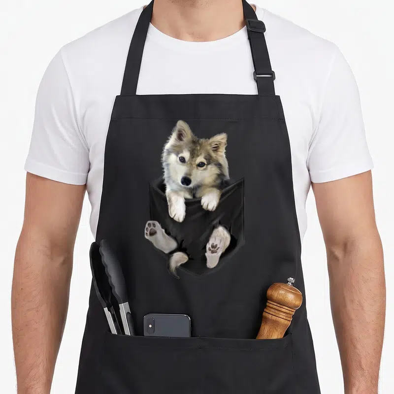 Tablier de cuisine noir avec illustration d'un chiot de loup brun sortant d'une poche noire avec ses pattes et sa queue.