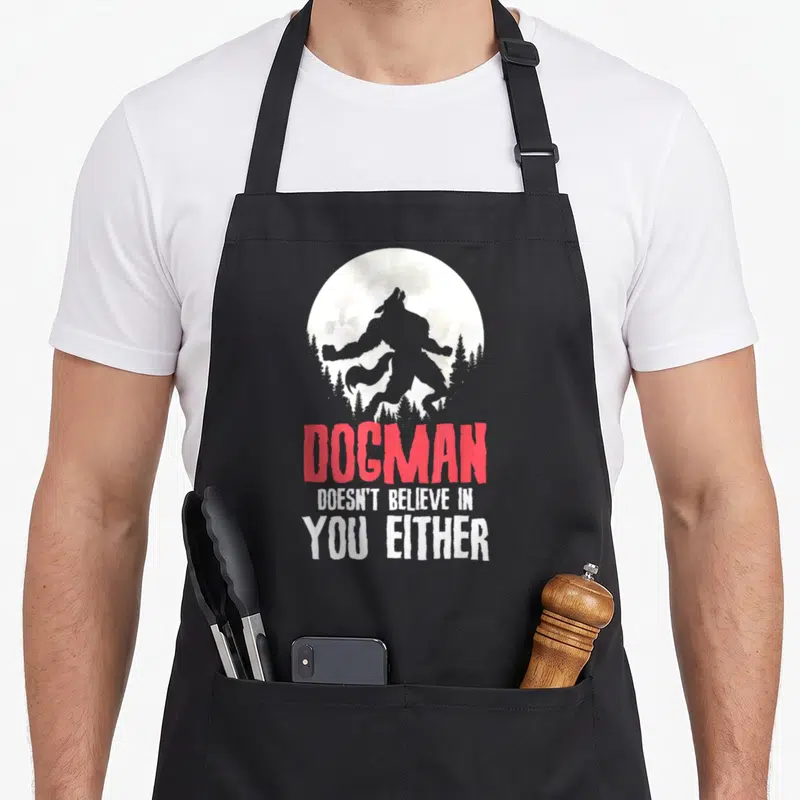 Tablier de cuisine noir avec silhouette Dogman et texte rouge et blanc sur fond lunaire.