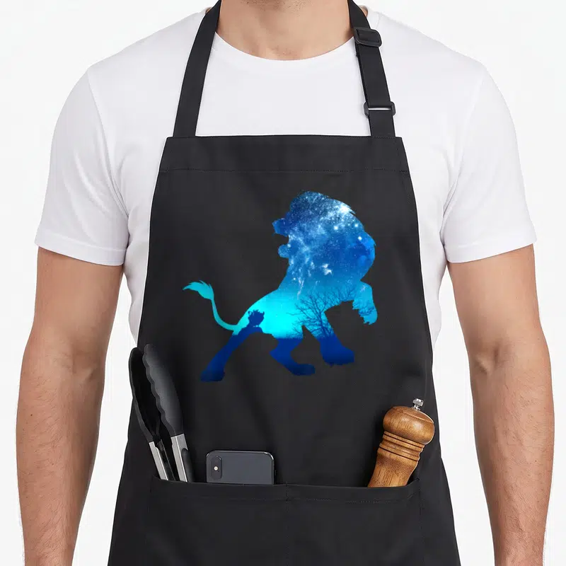 Tablier de cuisine noir avec silhouette de lion remplie d'un ciel étoilé bleu et d'arbres nus en contrebas.