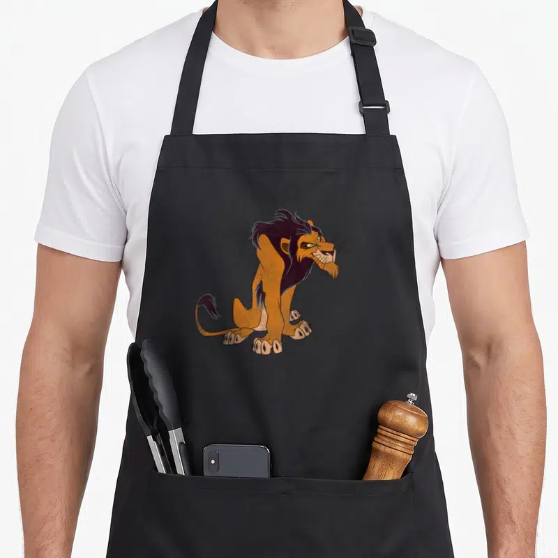 Tablier de cuisine noir avec illustration d'un lion orange à la mane noire et aux yeux verts, signature Scar en bas à gauche.