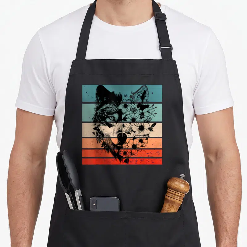 Tablier de cuisine noir avec tête de loup stylisée et motifs floraux sur fond de bandes horizontales bleues et orange.