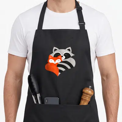 Tablier de cuisine noir avec un renard orange et un raton laveur gris s'enlacent tendrement.