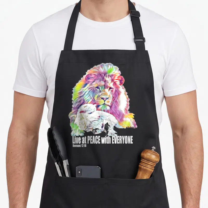 Tablier de cuisine noir avec illustration d'un lion aux couleurs vives protégeant un agneau blanc sous le texte Live at PEACE with EVERYONE.