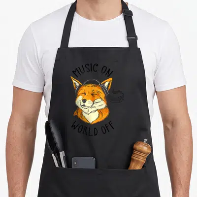 Tablier de cuisine noir avec illustration d'un renard souriant portant des écouteurs noirs et du texte en anglais.