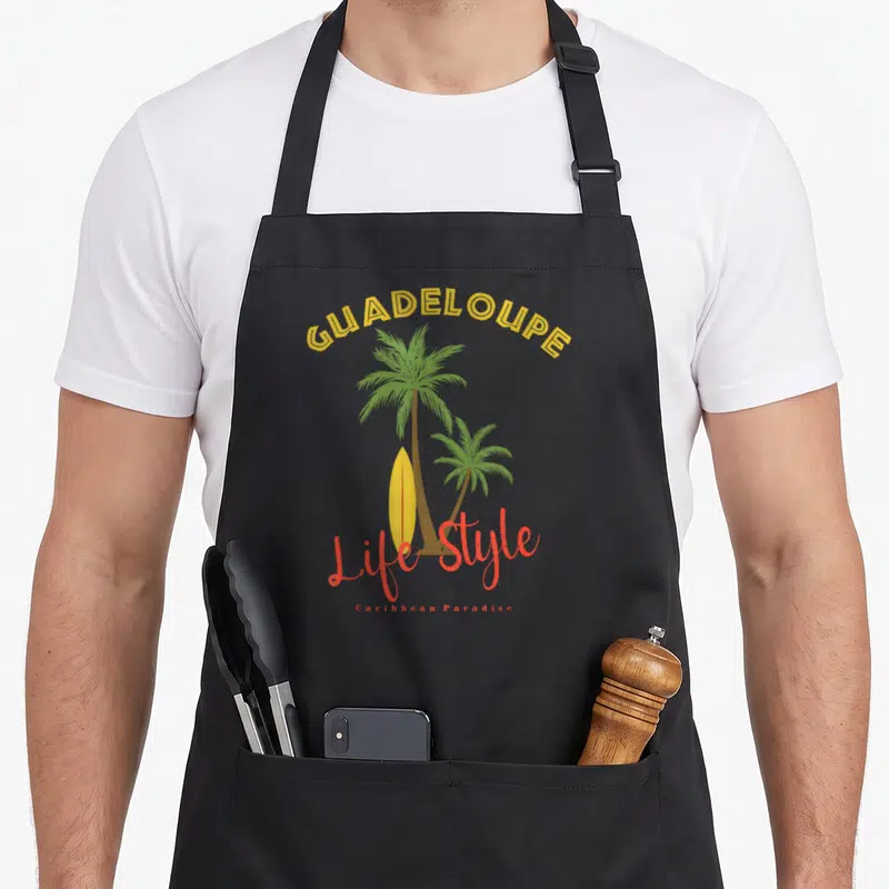 Tablier de cuisine noir avec illustration de palmiers, planche de surf et texte Guadeloupe Life Style en jaune et orange.