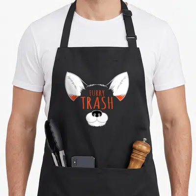 Tablier de cuisine noir avec illustration de renard aux oreilles blanches et texte Furry Trash en orange au centre.