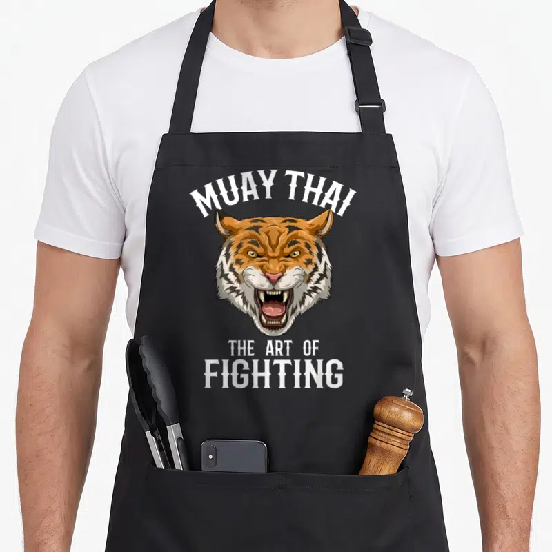 Tablier de cuisine noir avec tête de tigre rugissant et texte Muay Thai The Art of Fighting en blanc.