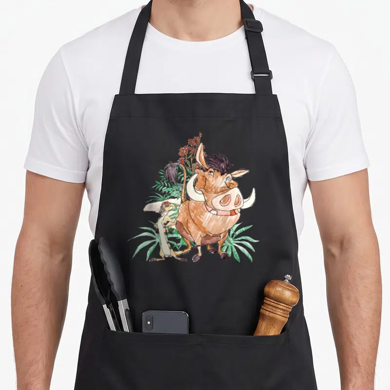 Tablier de cuisine noir avec illustration colorée de Timon et Pumba au milieu de plantes tropicales.