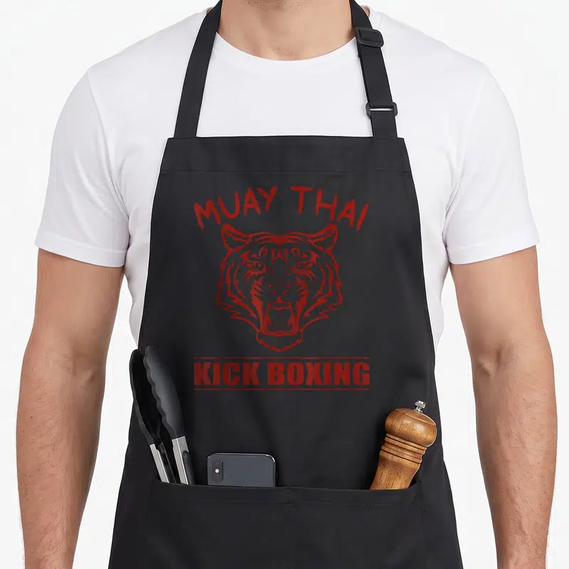 Tablier de cuisine noir avec tête de tigre rugissante et texte Muay Thai Kick Boxing en rouge.