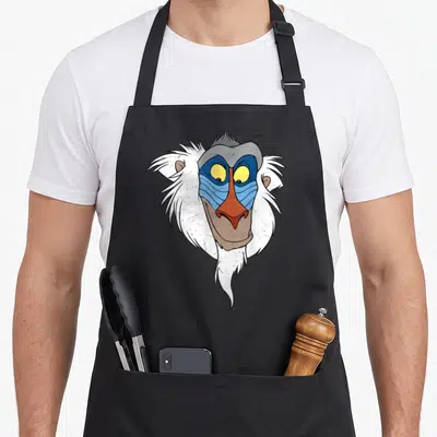 Tablier de cuisine noir avec le visage exagéré et coloré de Rafiki aux yeux jaunes et au museau rouge.
