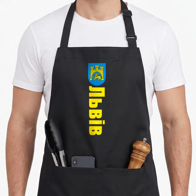 Tablier de cuisine noir avec le blason bleu et jaune de Lviv et un lion doré sous une forteresse.