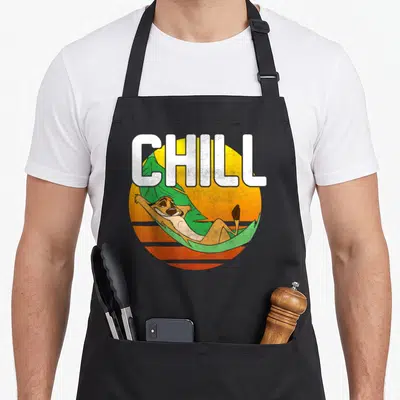 Tablier de cuisine noir avec un personnage de dessin animé allongé dans une feuille verte devant un soleil orange vintage.