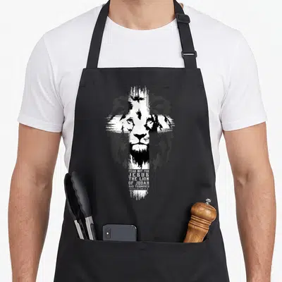 Tablier de cuisine noir avec tête de lion stylisée en croix blanche et texte Fear not for Jesus The Lion of Judah has triumphed.