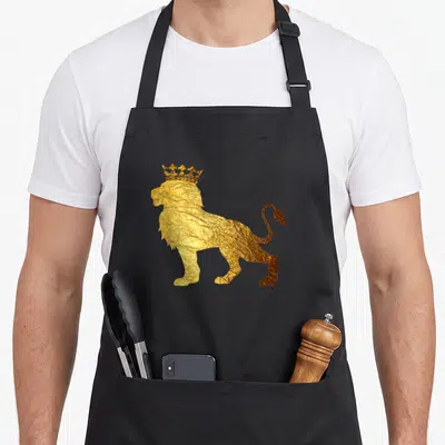 Tablier de cuisine noir avec silhouette de lion africain doré et couronne en relief texturé sur le devant.