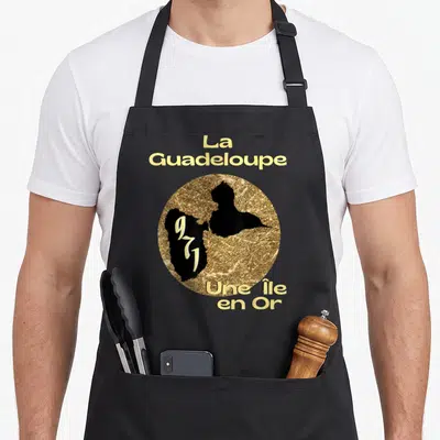 Tablier de cuisine noir avec motif circulaire doré et noir représentant la carte de La Guadeloupe et le texte Une Île en Or.