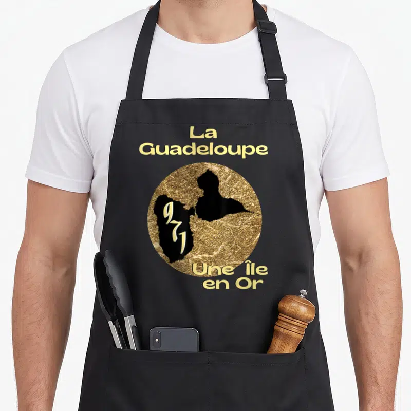 Tablier de cuisine noir avec motif circulaire doré et noir représentant la carte de La Guadeloupe et le texte Une Île en Or.