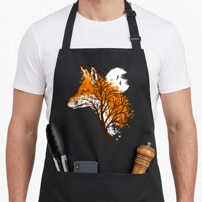 Tablier de cuisine noir avec un renard stylisé en orange et blanc, intégré à un arbre aux branches sombres devant une lune pleine.