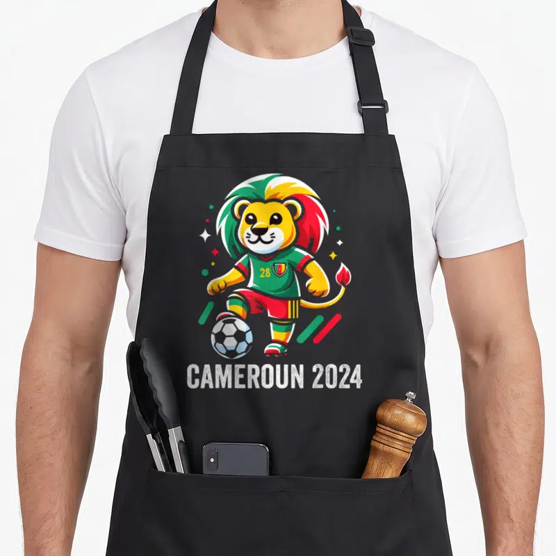 Tablier de cuisine noir avec un lion footballeur aux couleurs du Cameroun et le texte Cameroun 2024 en bas.
