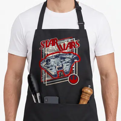 Tablier de cuisine noir avec illustration vintage du vaisseau spatial et logo de la Rébellion en rouge et bleu.