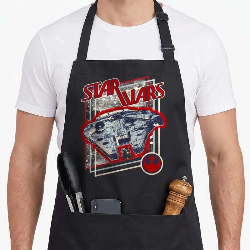 Tablier de cuisine noir avec illustration vintage du vaisseau spatial et logo de la Rébellion en rouge et bleu.