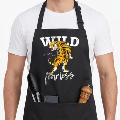Tablier de cuisine noir avec illustration d'un tigre orange et des mots WILD fearless printed in white.