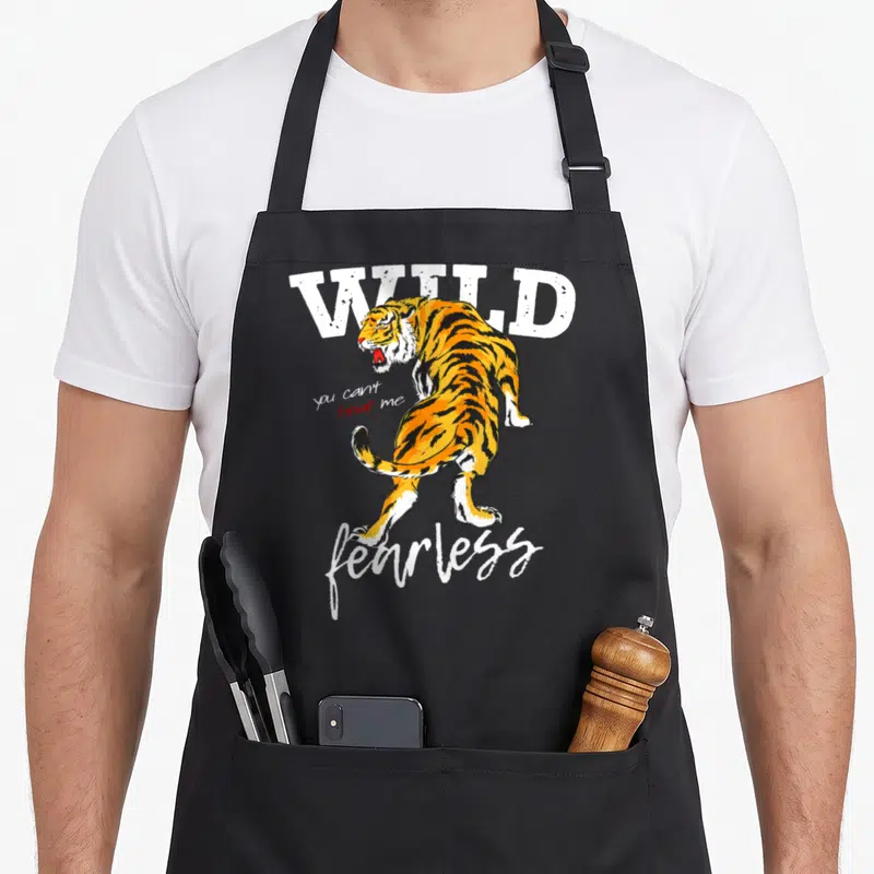 Tablier de cuisine noir avec illustration d'un tigre orange et des mots WILD fearless printed in white.