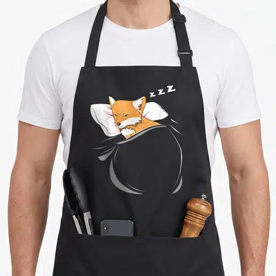 Tablier de cuisine noir avec illustration d'un renard dormant sur un oreiller sous une couverte grise.