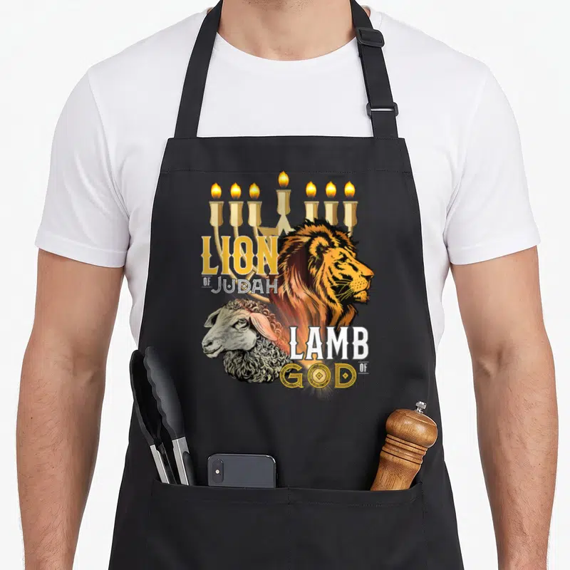 Tablier de cuisine noir avec illustration d'un lion et d'un agneau sous un menorah doré, texte Lion of Judah et Lamb of God.