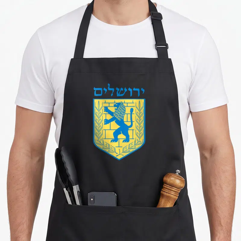 Tablier de cuisine noir avec l'emblème jaune et bleu du lion de Jérusalem et des caractères hébraïques.