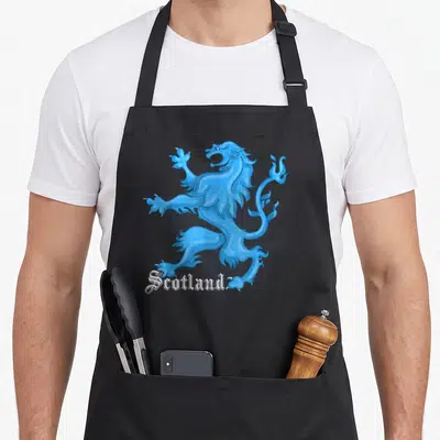 Tablier de cuisine noir avec illustration bleue d'un lion écossais rampant et le texte Scotland en typographie gothique blanche.