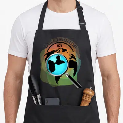 Tablier de cuisine noir avec illustration d'une loupe sur la carte de la Guadeloupe 971 et un fond de globe terrestre.