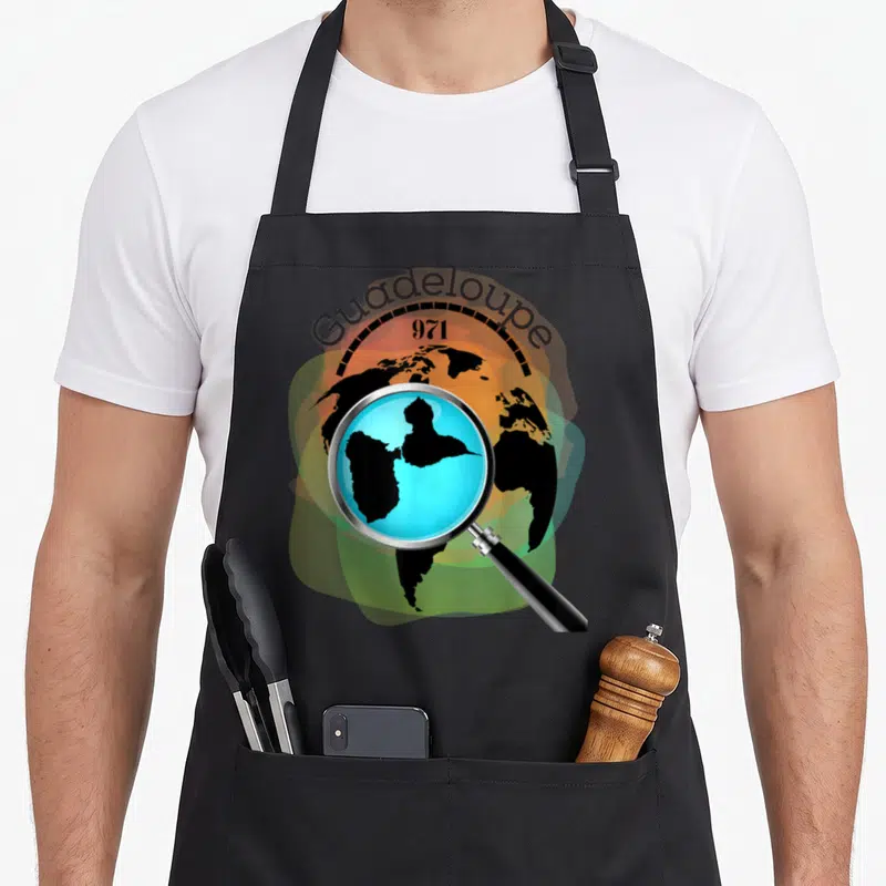 Tablier de cuisine noir avec illustration d'une loupe sur la carte de la Guadeloupe 971 et un fond de globe terrestre.