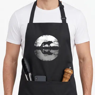 Tablier de cuisine noir avec illustration circulaire montrant un renard et son reflet dans l'eau au milieu d'arbres nus.