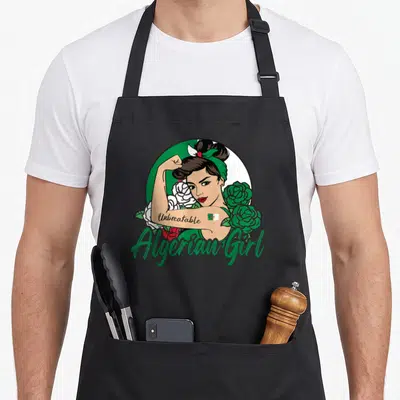 Tablier de cuisine noir avec une illustration dAlgerian Girl aux bras forts entourée de roses et du drapeau algérien.