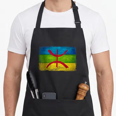 Tablier de cuisine noir avec le drapeau amazigh aux couleurs bleu vert et jaune et le signe Tifinagh rouge au centre.