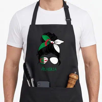 Tablier de cuisine noir avec illustration d'une femme au foulard et lunettes reflétant le drapeau Algérie et le mot Algeria.