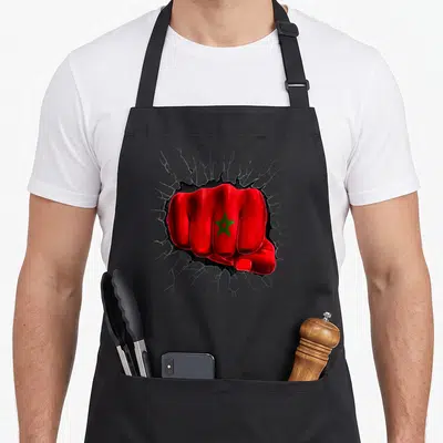 Tablier de cuisine noir avec un poing rouge percant un mur affichant une étoile verte au centre des doigts.